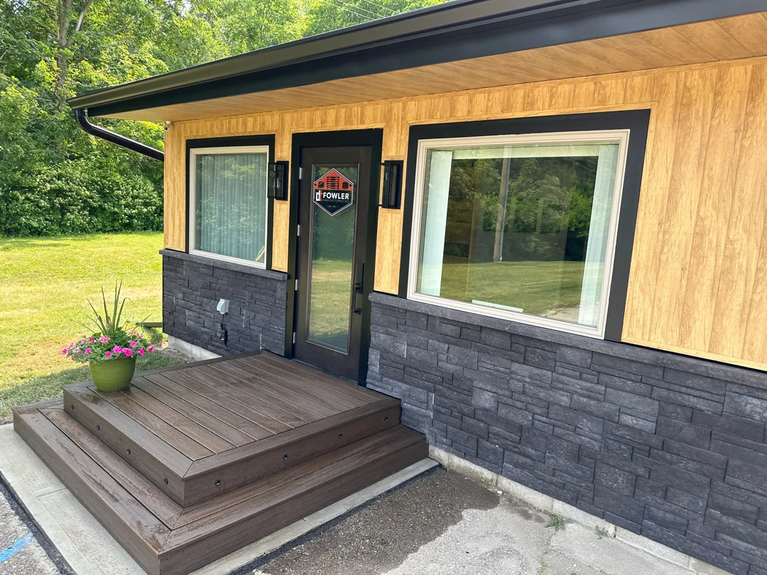 Custom wood and stone siding with black trim and a glass entry door installed by The Exterior Zone in Metamora, MI.