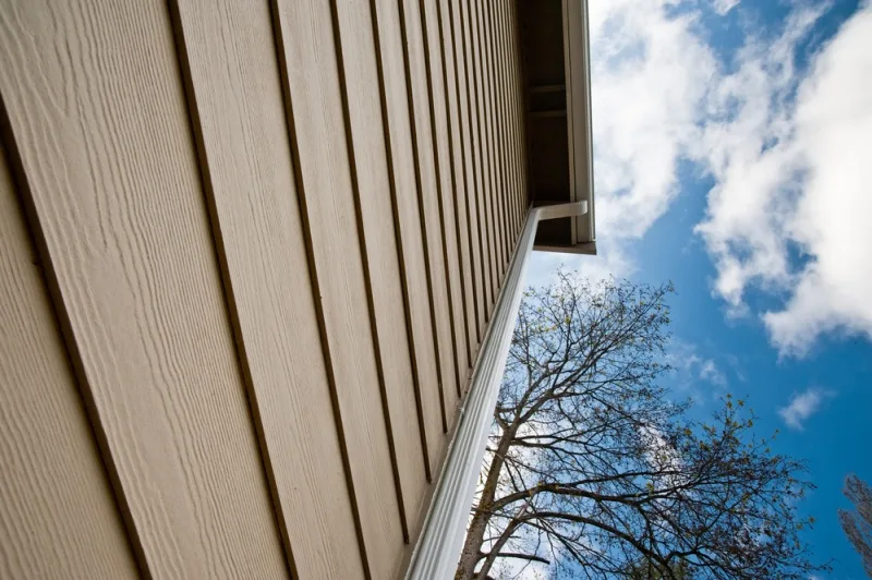 Close-up of professionally installed beige fiber cement siding by The Exterior Zone in Metamora, MI, with a clear blue sky in the background.